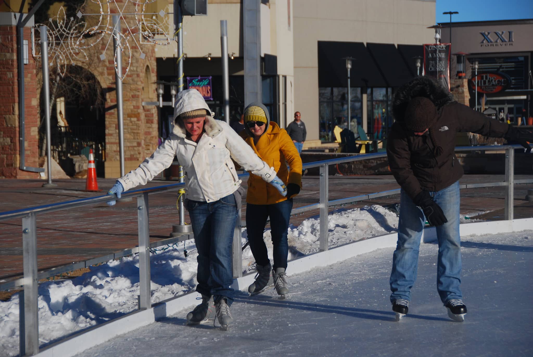 3 people ice skating on an outdoor rink
