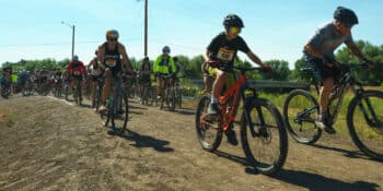 Pack of bike riders on a sunny day and a dirt trail during the Rio Trio race in Alamosa.