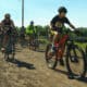 Pack of bike riders on a sunny day and a dirt trail during the Rio Trio race in Alamosa.
