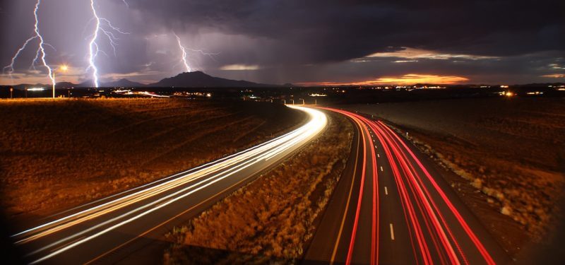 Long exposure shot of cars on the highway with lightning in the background