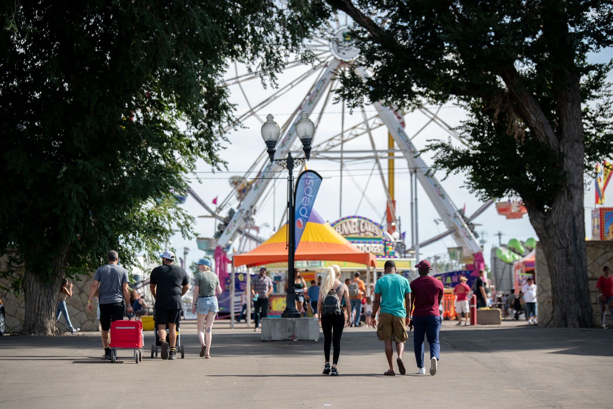 People walking into a state fair with a huge ferris wheel and food booths