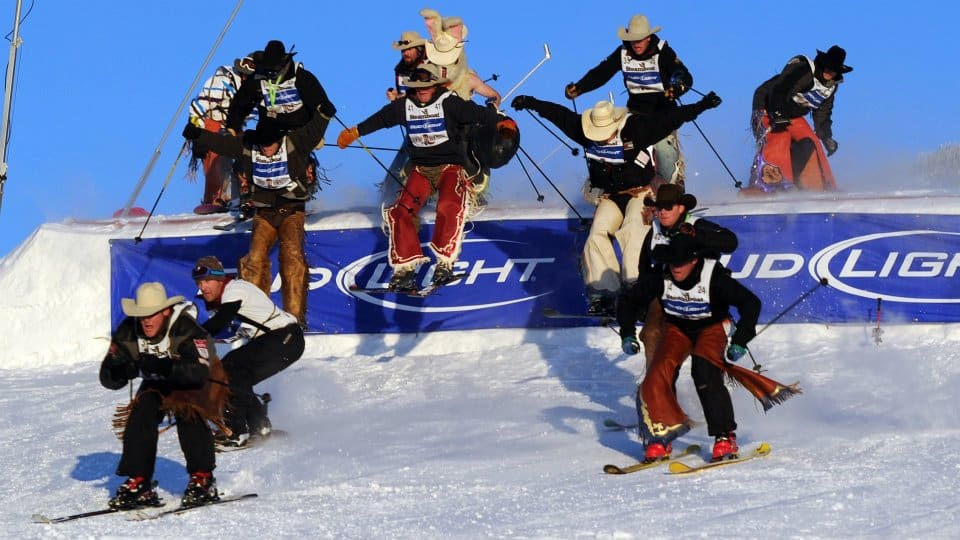 Group of cowboys in western garb on skis making their way off a small ski jump at the Cowboy Downhill event in Steamboat Springs