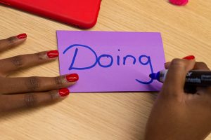 Person writing 'Doing' on a purple Post-it note