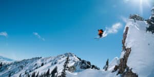 Skier in a red jacket on Icelantic Skis sending it off a huge jump on a bluebird skies day