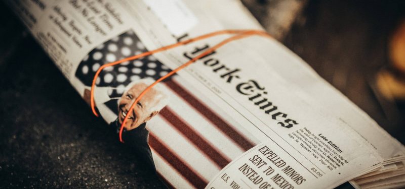 A rolled and banded copy of The New York Times with President Joe Biden on the front page