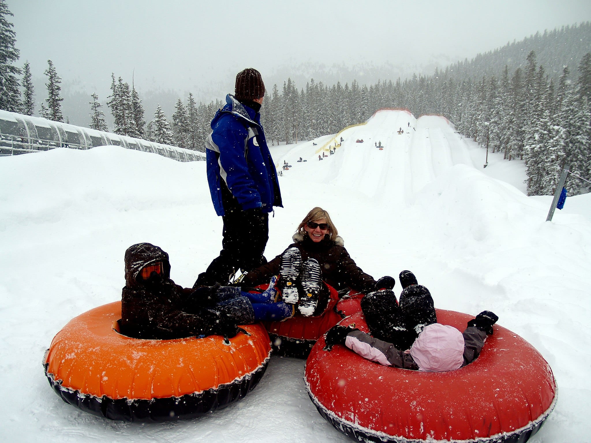 3 people in snow tubes and person standing over them at the bottom of the hill