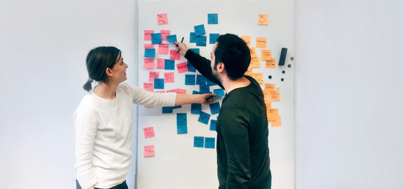 Two people collaborating on a whiteboard with sticky notes