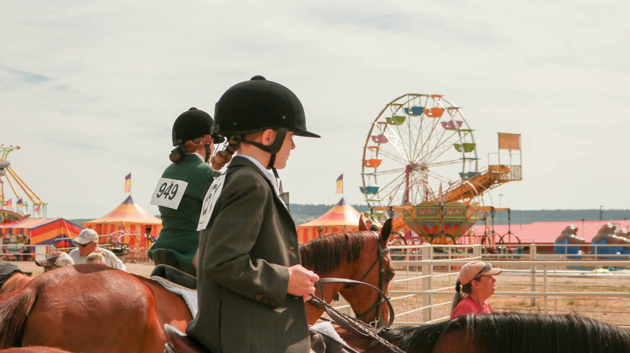 Two young girls on horses with fairgrounds in the background