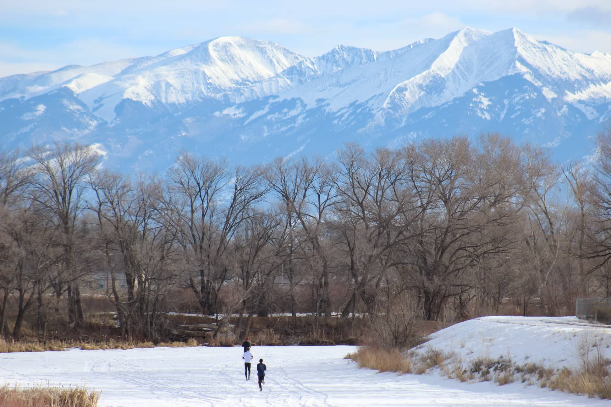 People running on a a snowy, frozen over river for the Rio Frio Ice Fest with large mountains in the background in Alamosa