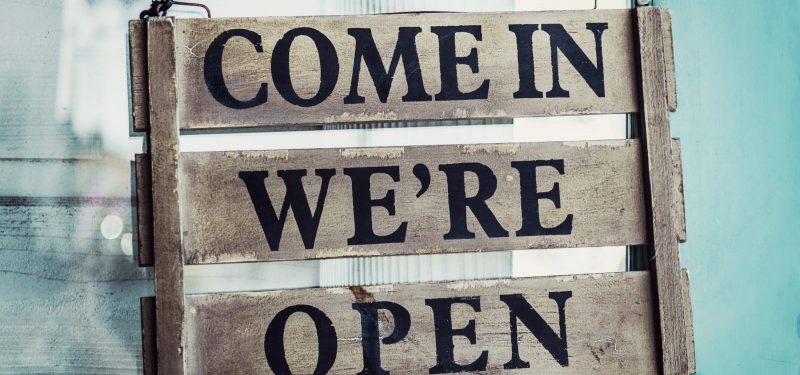 Shop's come in we're open sign on a blue door