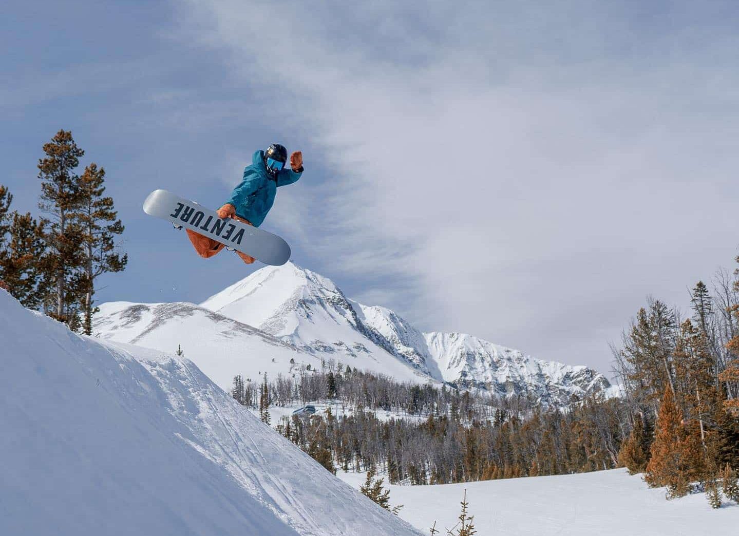 Snowboarder in blue jacket in the air after a jump on a white Venture snowboard